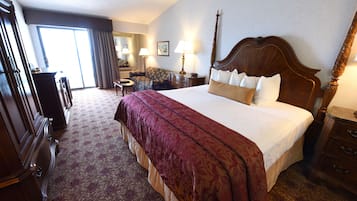 A hotel room with a large bed, a desk, a chair, a dresser, and a view of the outside.