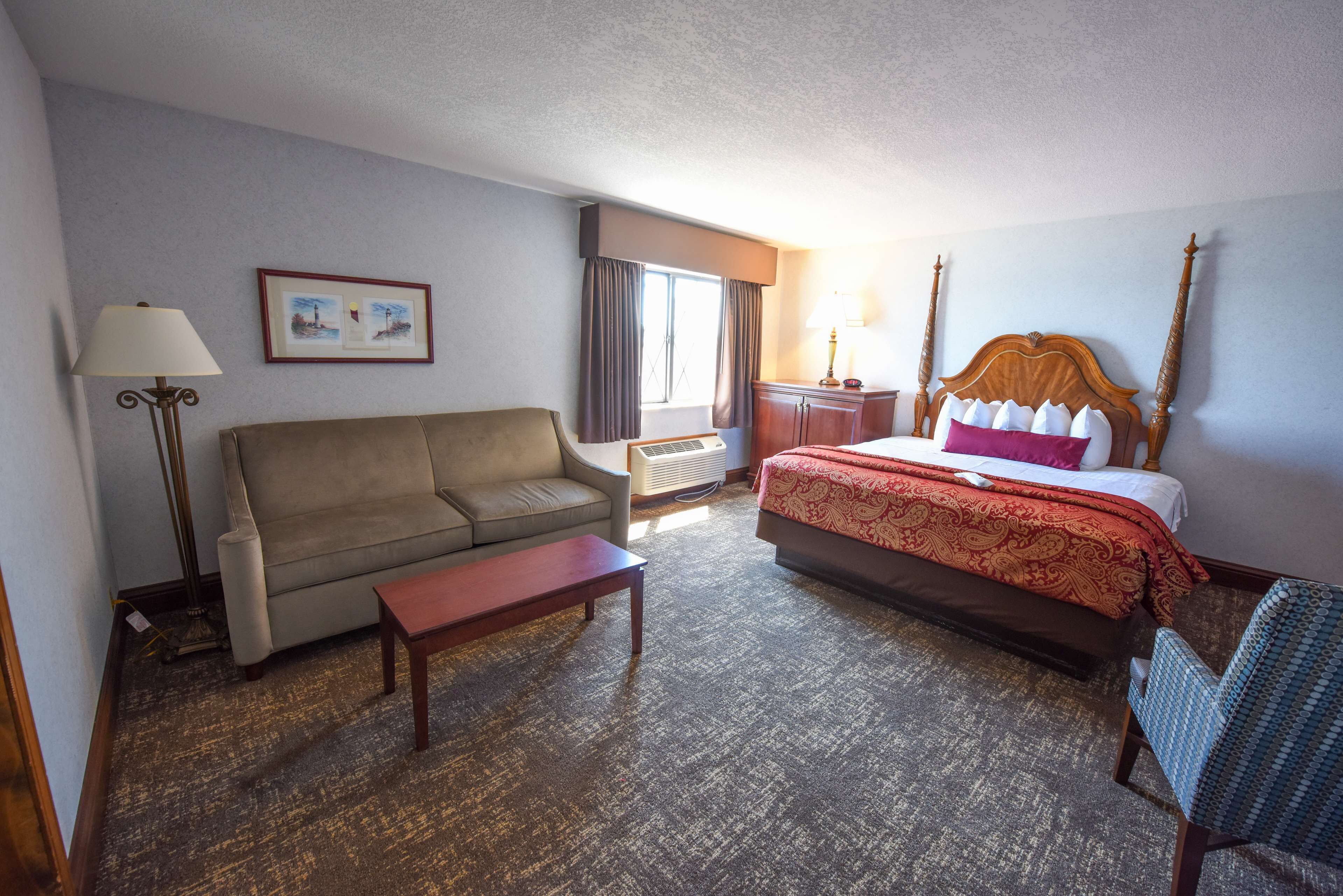 Une chambre d’hôtel avec un lit, un canapé, une petite table, une lampe et un tableau au mur.