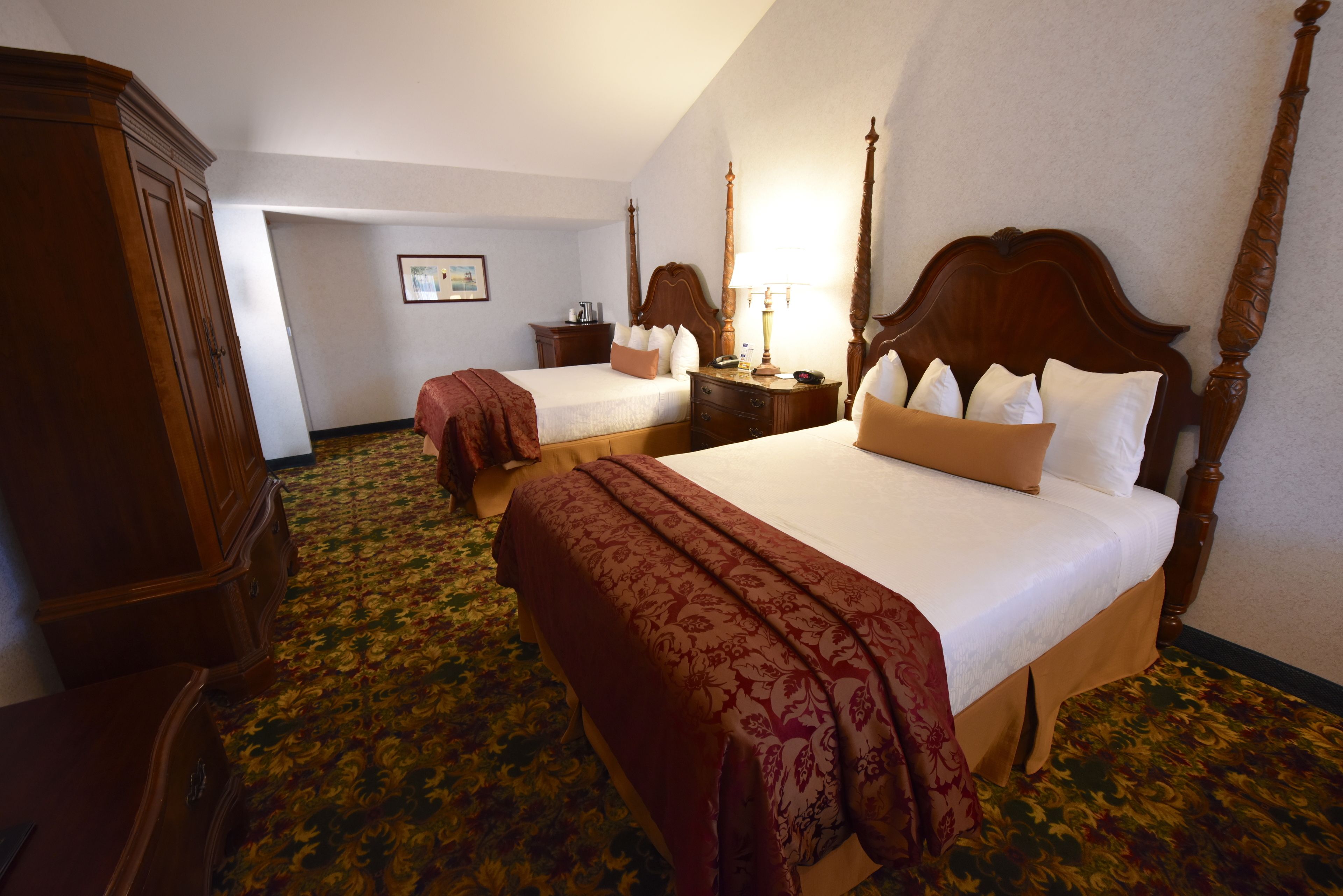 Habitación de hotel con dos camas, un armario de madera, una mesita de noche y una lámpara.