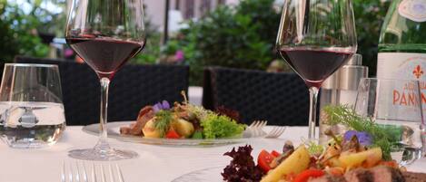 A dining table with plates of food, wine glasses, and a bottle of PANNIN.