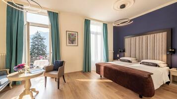 Una habitación de hotel con una cama, una silla, una mesa, un ventanal con cortinas, un radiador y una lámpara fijada a la pared.