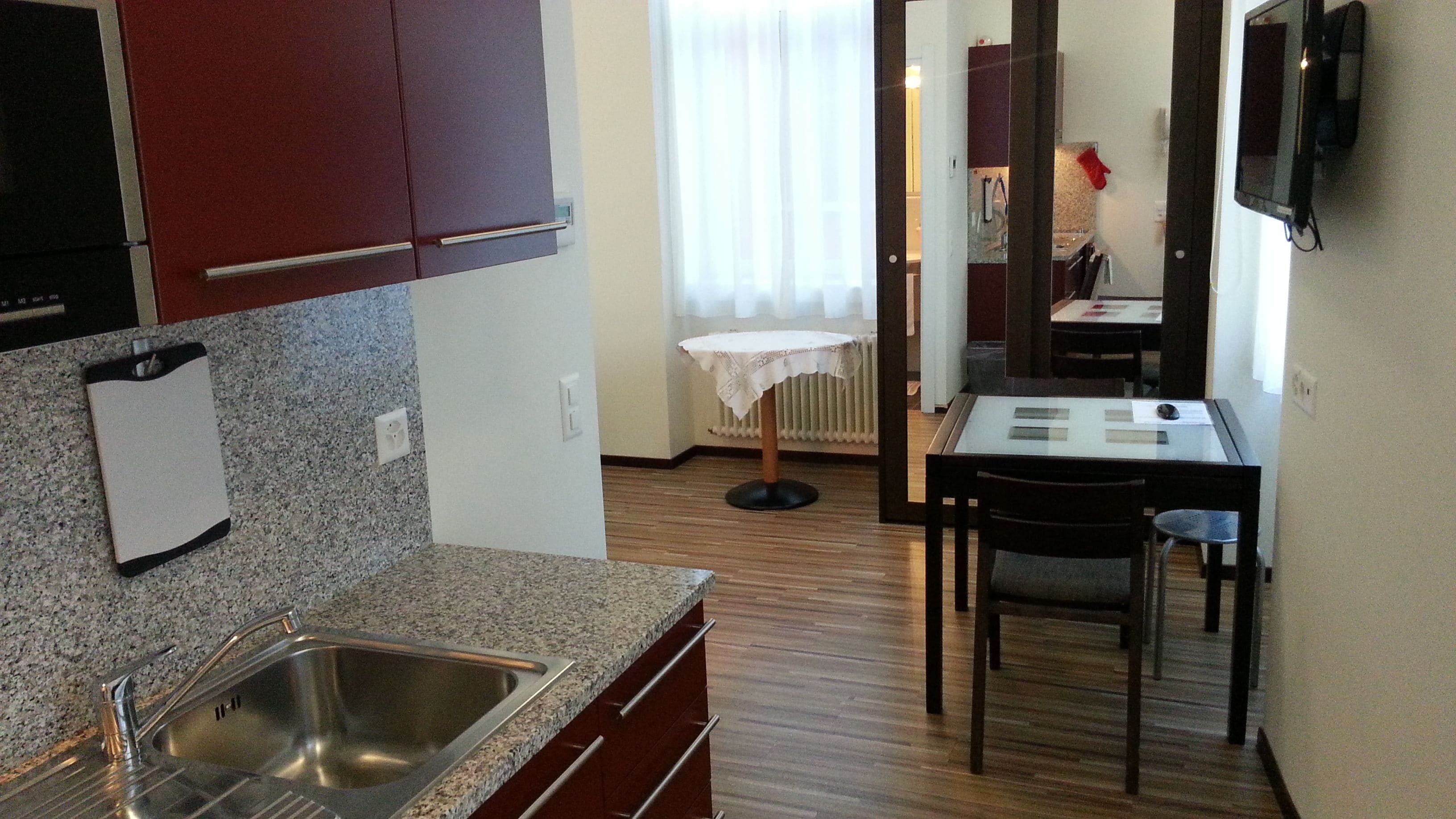 Una cocina compacta con encimeras de granito, un lavamanos de acero inoxidable y armarios de madera.