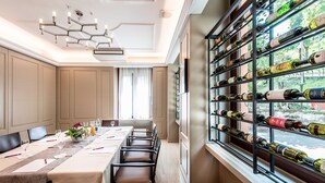 Un coin repas avec une longue table dressée pour le repas, un meuble à vin rempli de bouteilles et une vue par la fenêtre.