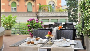 Un espace de restauration en plein air avec des tables dressées pour le petit-déjeuner, comprenant un panier de fruits, des assiettes, des tasses et des viennoiseries.