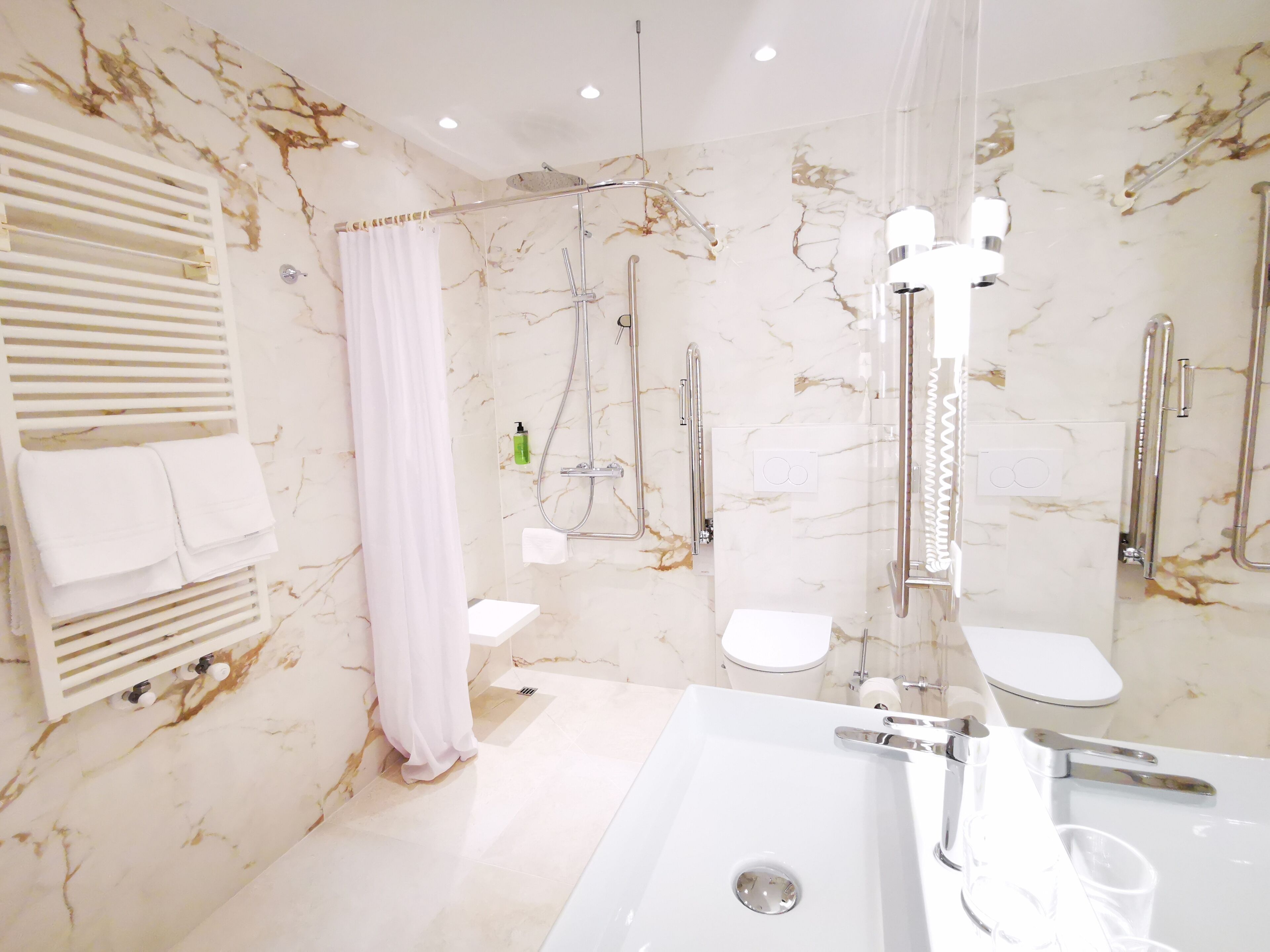 Un baño moderno con un lavamanos grande de color blanco, una ducha con cerramiento de vidrio, un inodoro y un perchero para toallas.