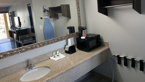 Une salle de bain dotée d’un comptoir en granit, d’un lavabo, d’un grand miroir orné d’un cadre floral, d’une machine à café et d’un porte-serviettes.