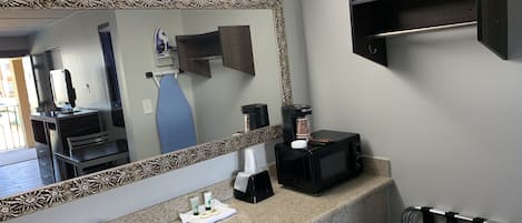 A bathroom with a granite countertop, a sink, a large mirror with a floral frame, a coffee maker, and a towel rack.