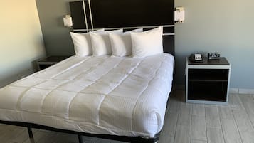 Una cama bien tendida con ropa blanca, cabecera negra y dos mesitas de noche con un reloj y un teléfono.