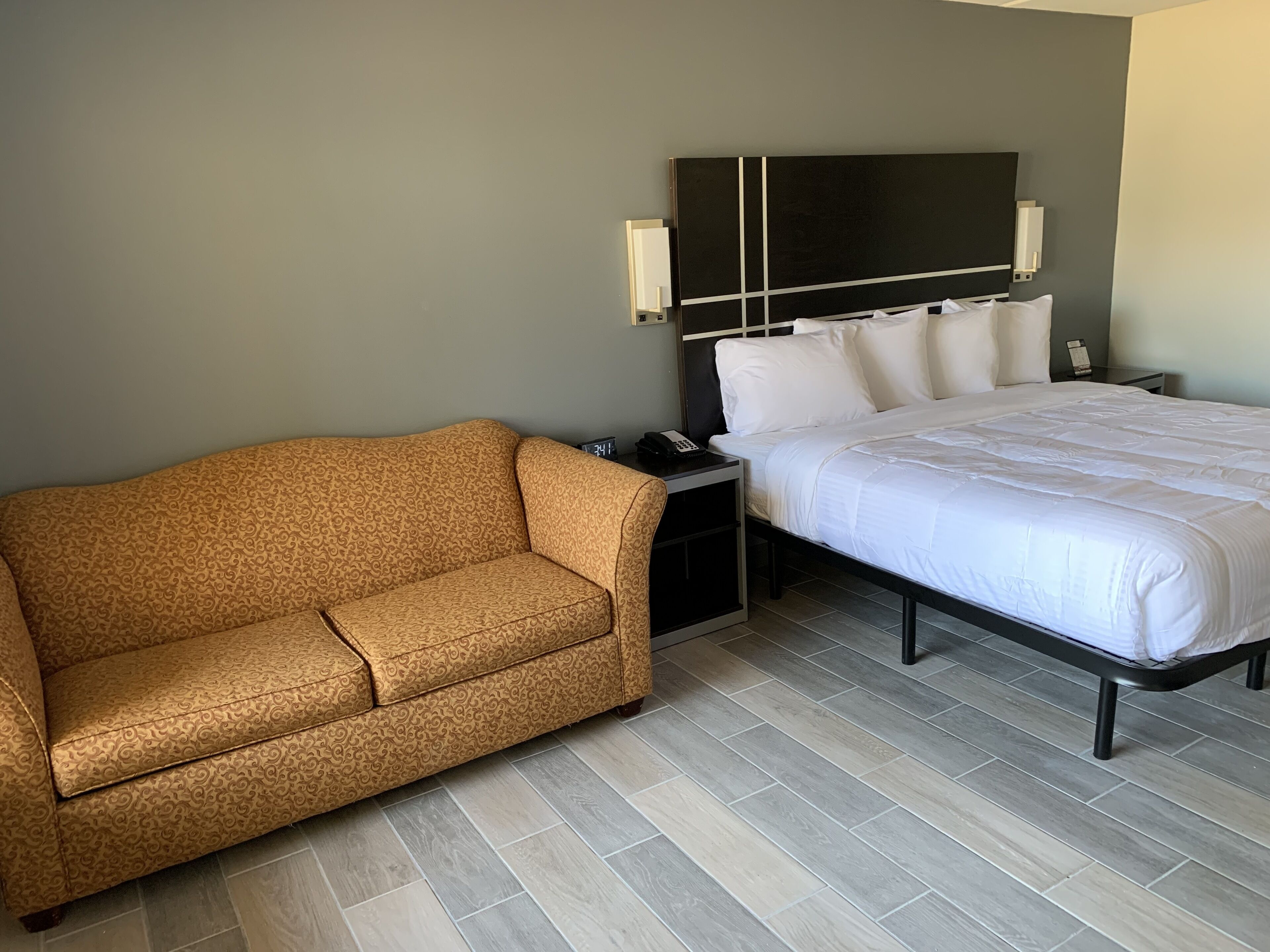 A hotel room with a bed, a sofa, a nightstand, and a wall-mounted TV.