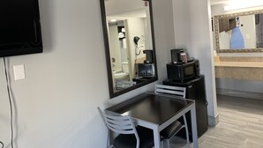 Une chambre d’hôtel équipée d’une télévision, d’un grand miroir, d’une petite table avec une chaise, d’un four à micro-ondes et d’une machine à café.