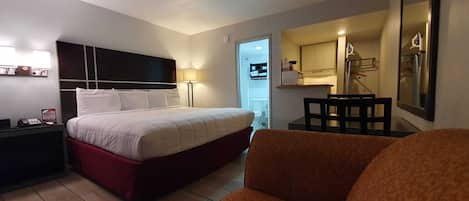 Habitación de hotel con cama, escritorio, silla y una pequeña cocina.