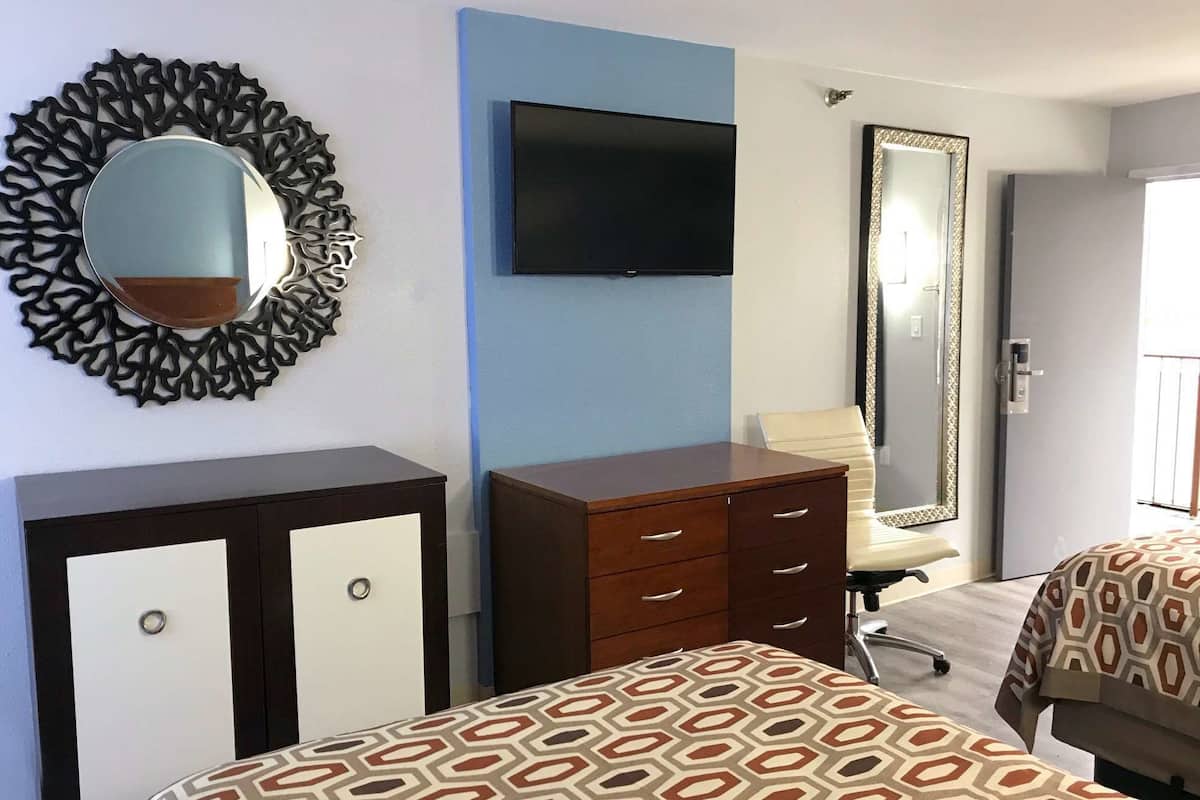 A hotel room with a bed, a dresser, a TV, a mirror, and a door leading to a balcony.