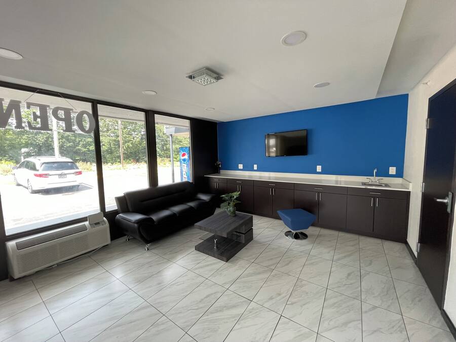 A modern interior with a black leather sofa, a small blue stool, a coffee table, and a kitchen area with dark cabinets and a white countertop.