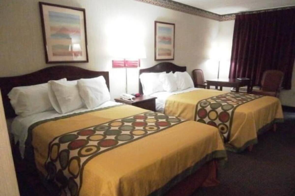 A hotel room with two beds, a desk, a chair, and two framed pictures on the wall.