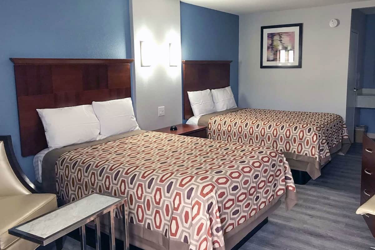 A hotel room with two beds, a bedside table, a chair, and a framed picture on the wall.