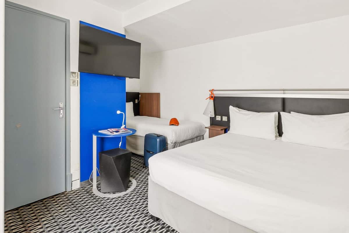 Habitación de hotel con una cama grande, una cama más pequeña, un escritorio con silla, pared azul y una puerta.
