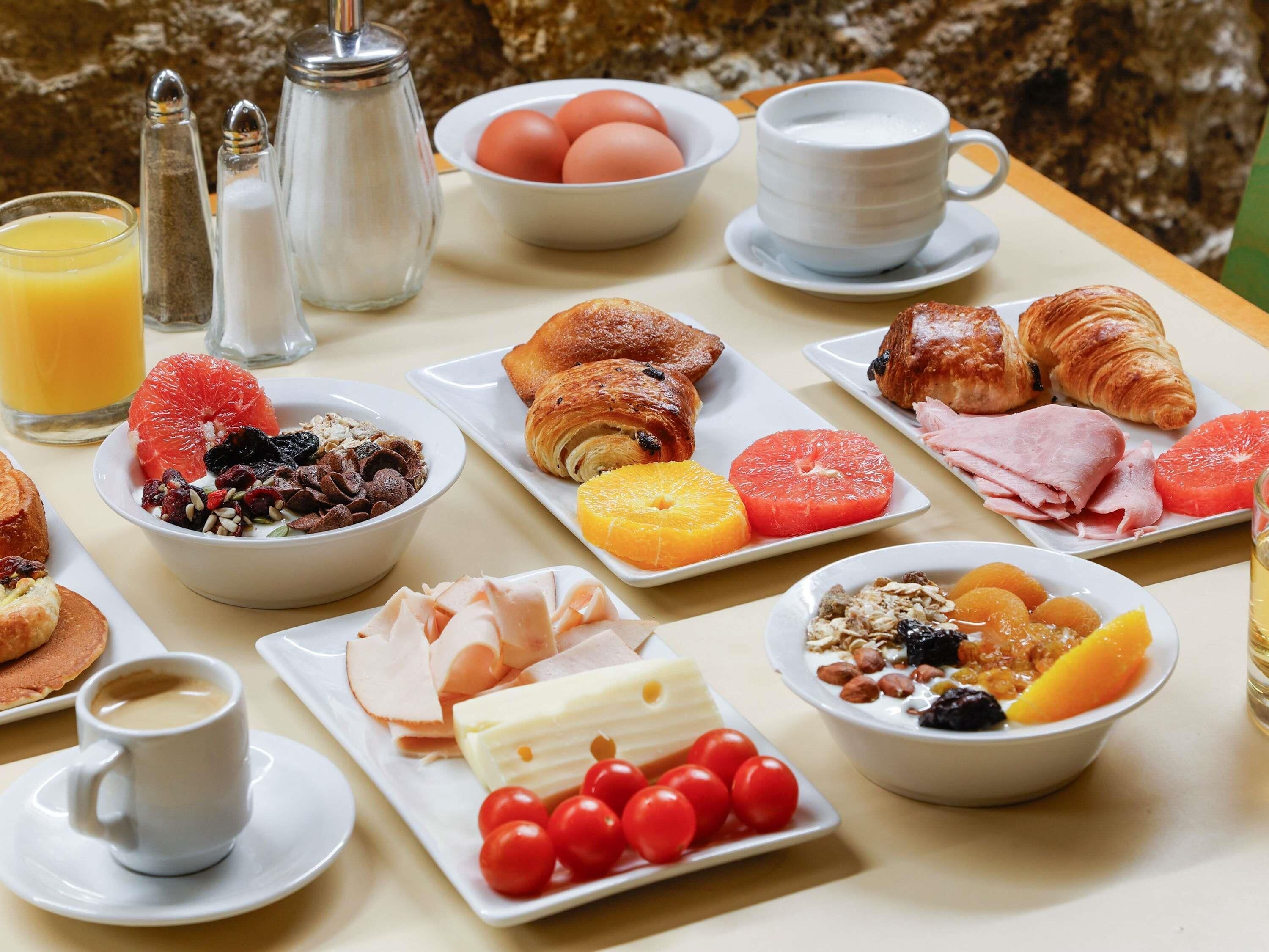 A breakfast table with various food items, including croissants, eggs, and fruits.