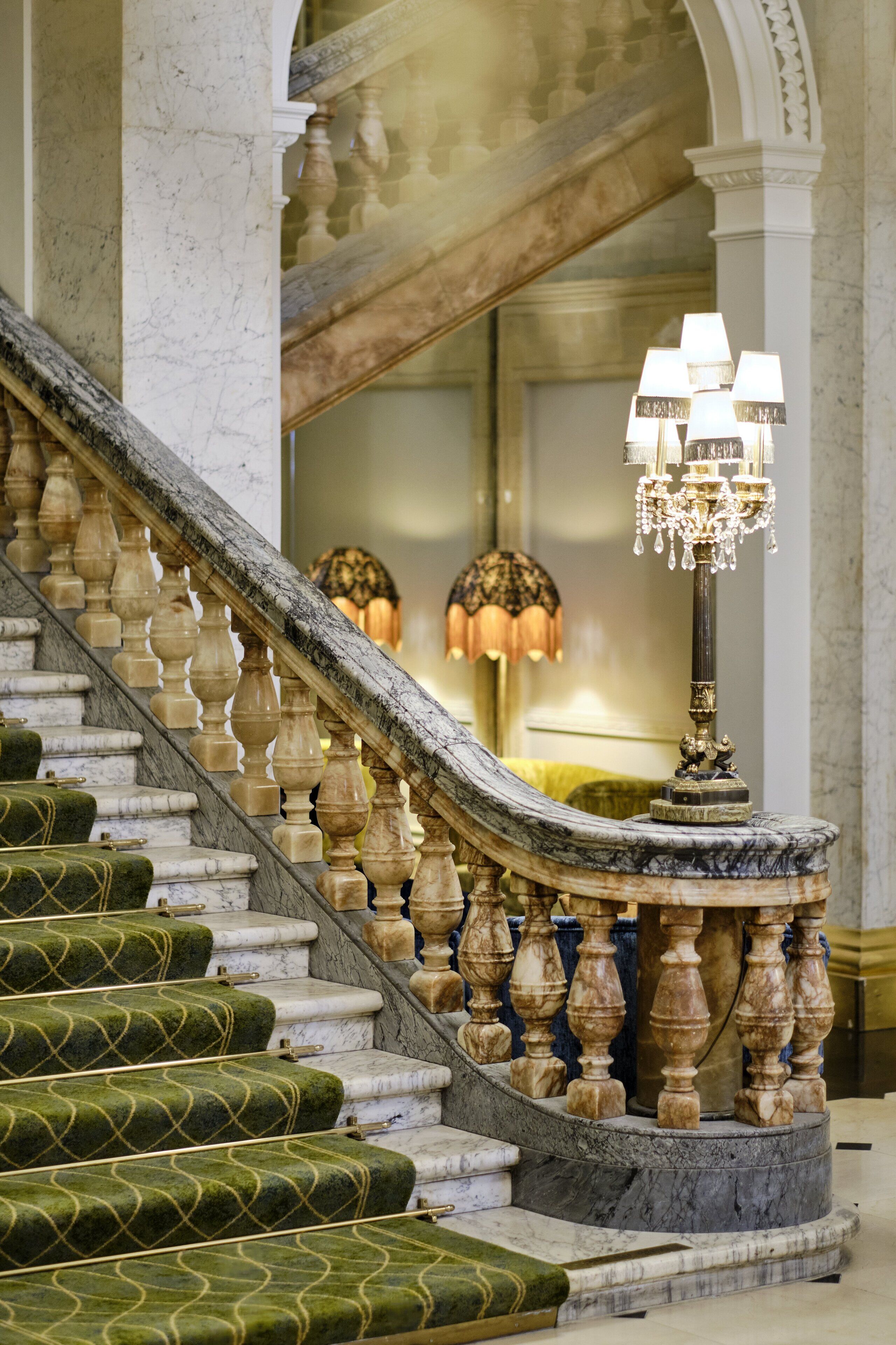 Eine prächtige Treppe mit Marmorstufen und aufwendiger Balustrade, die zu einem Raum mit einer Chandelüstere und einem großen Spiegel führt.