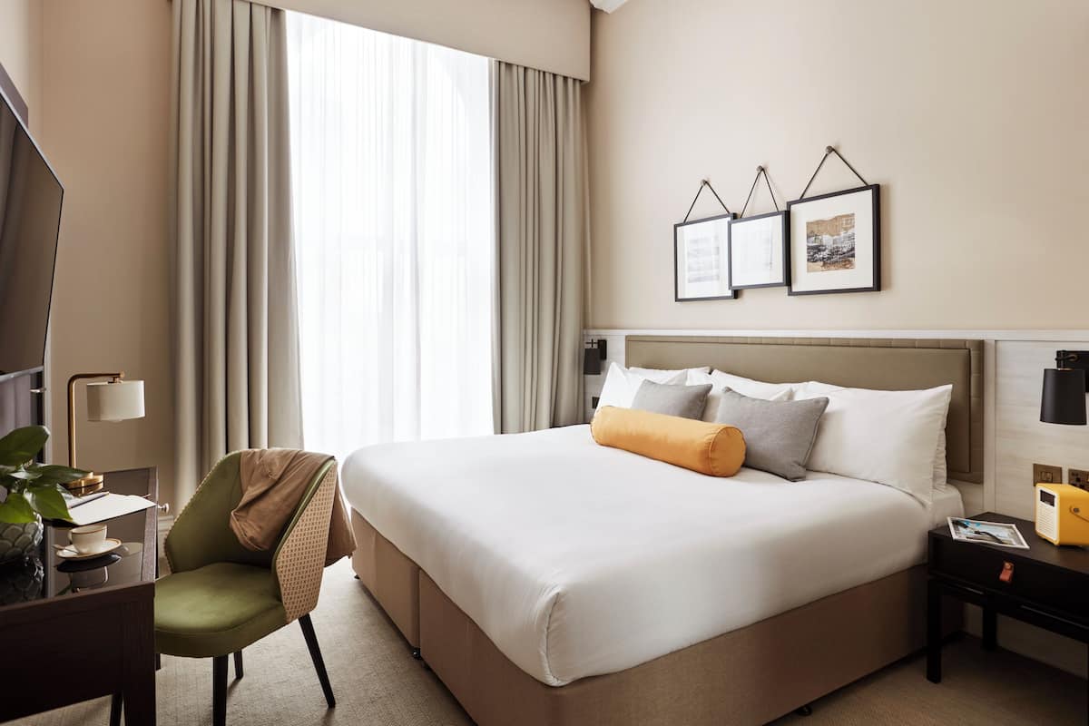 A hotel room with a large bed, a desk with a chair, a TV, and a window with curtains.
