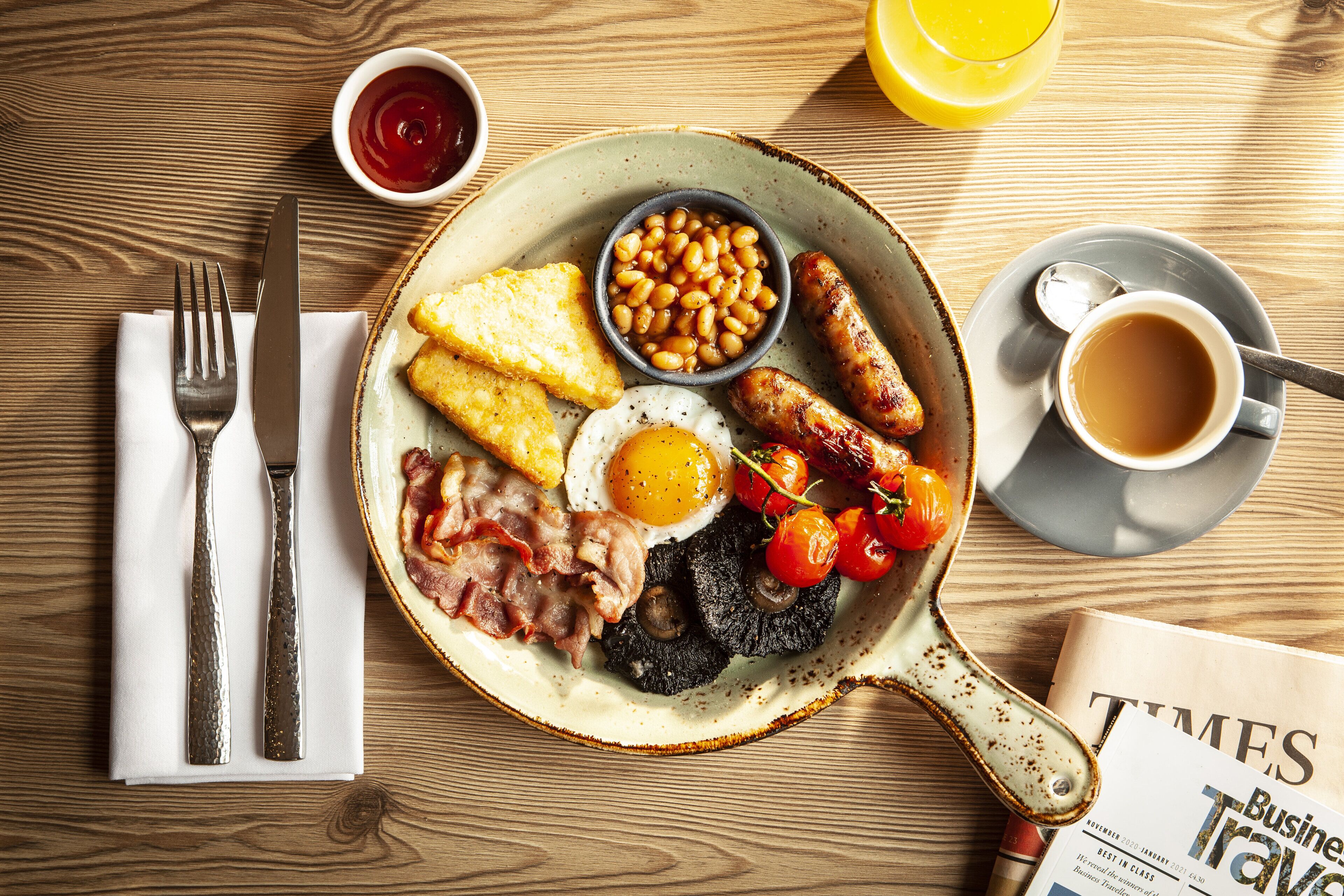 A breakfast plate with eggs, bacon, sausages, beans, toast, and tomatoes on a wooden table.