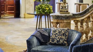 A lobby with a blue sofa, a small table with a cup and magazine, a large floral arrangement, and a grand staircase.