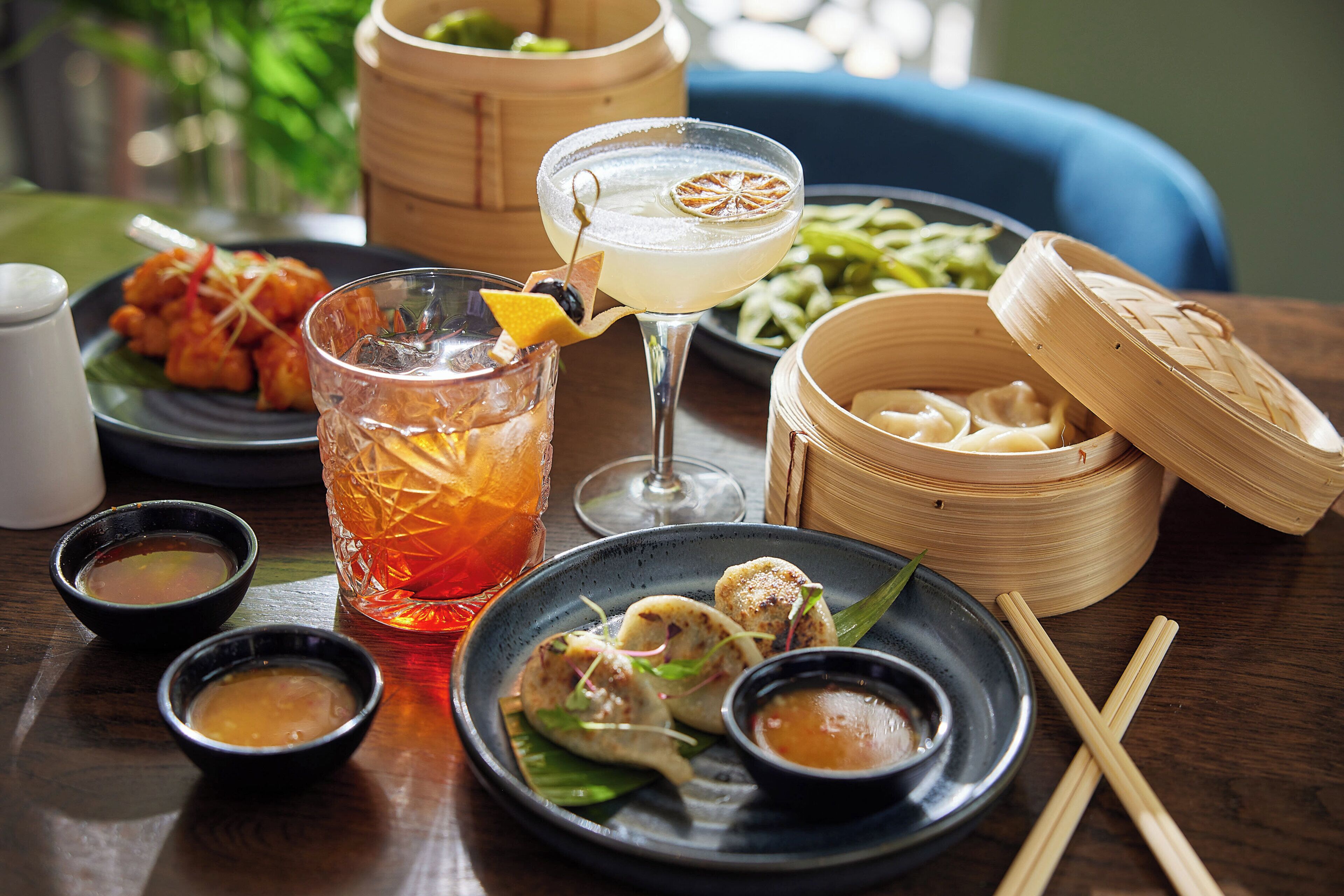 Une table avec des plats de dim sum, un cocktail et du thé.