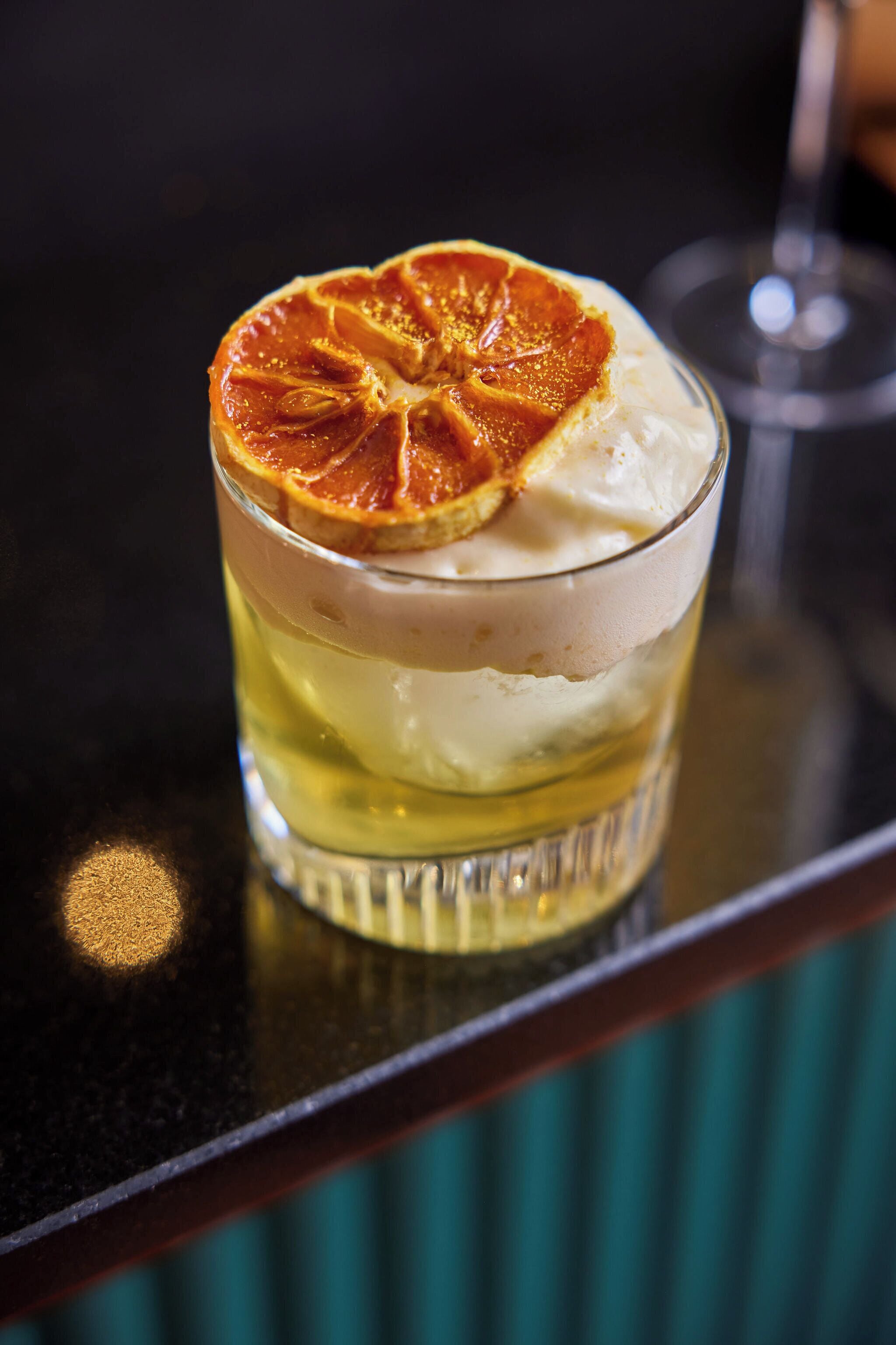 Un vaso con bebidas en capas y una rodaja de naranja deshidratada encima.