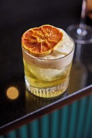 Ein Glas mit schichtweise angeordneten Getränken und einer getrockneten Orangenscheibe obenauf.