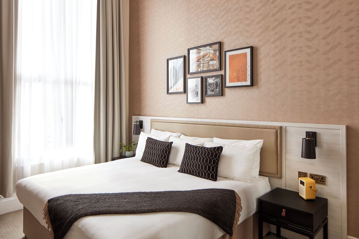 A hotel room with a large bed, a bedside table with a lamp, and a wall-mounted artwork.