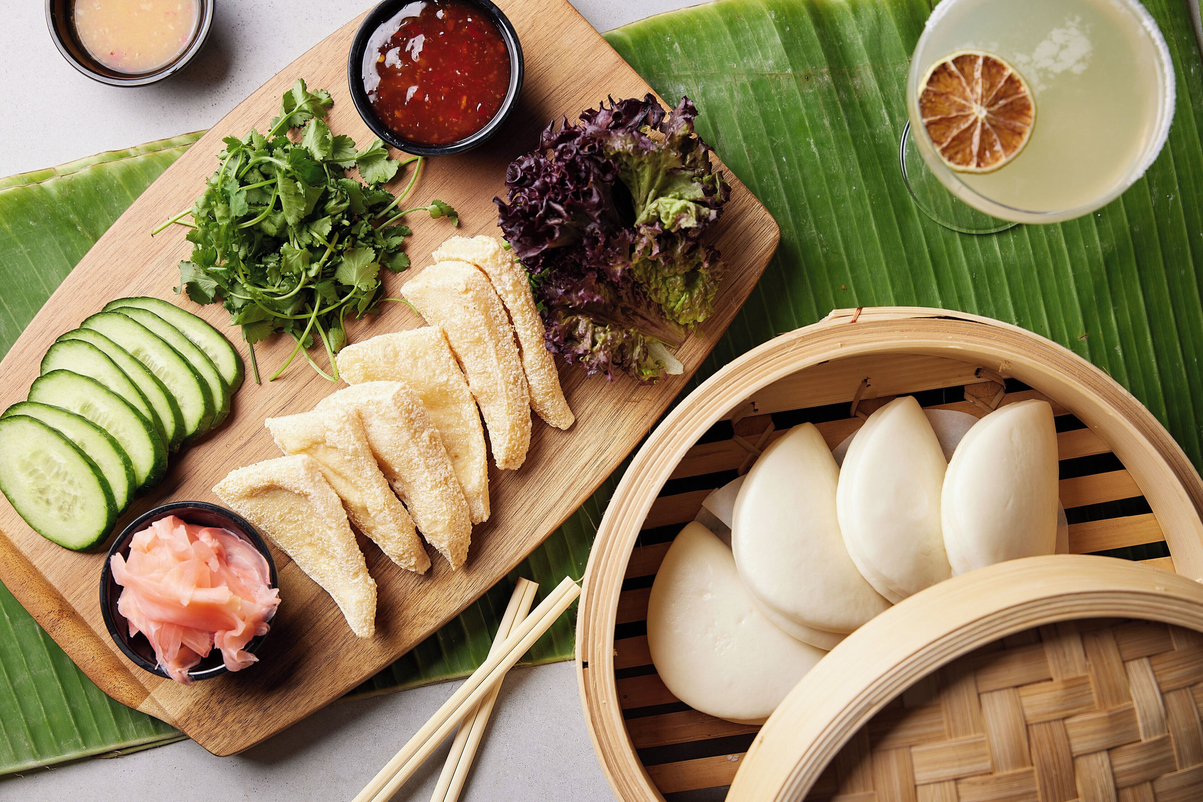 A wooden board with sliced cucumbers, pickled vegetables, and a bowl of sauce.