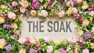 A wall with "THE SOAK" and "BAR LOUNGE KITCHEN" text surrounded by a variety of flowers.