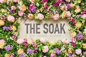 A wall with "THE SOAK" and "BAR LOUNGE KITCHEN" text surrounded by a variety of flowers.