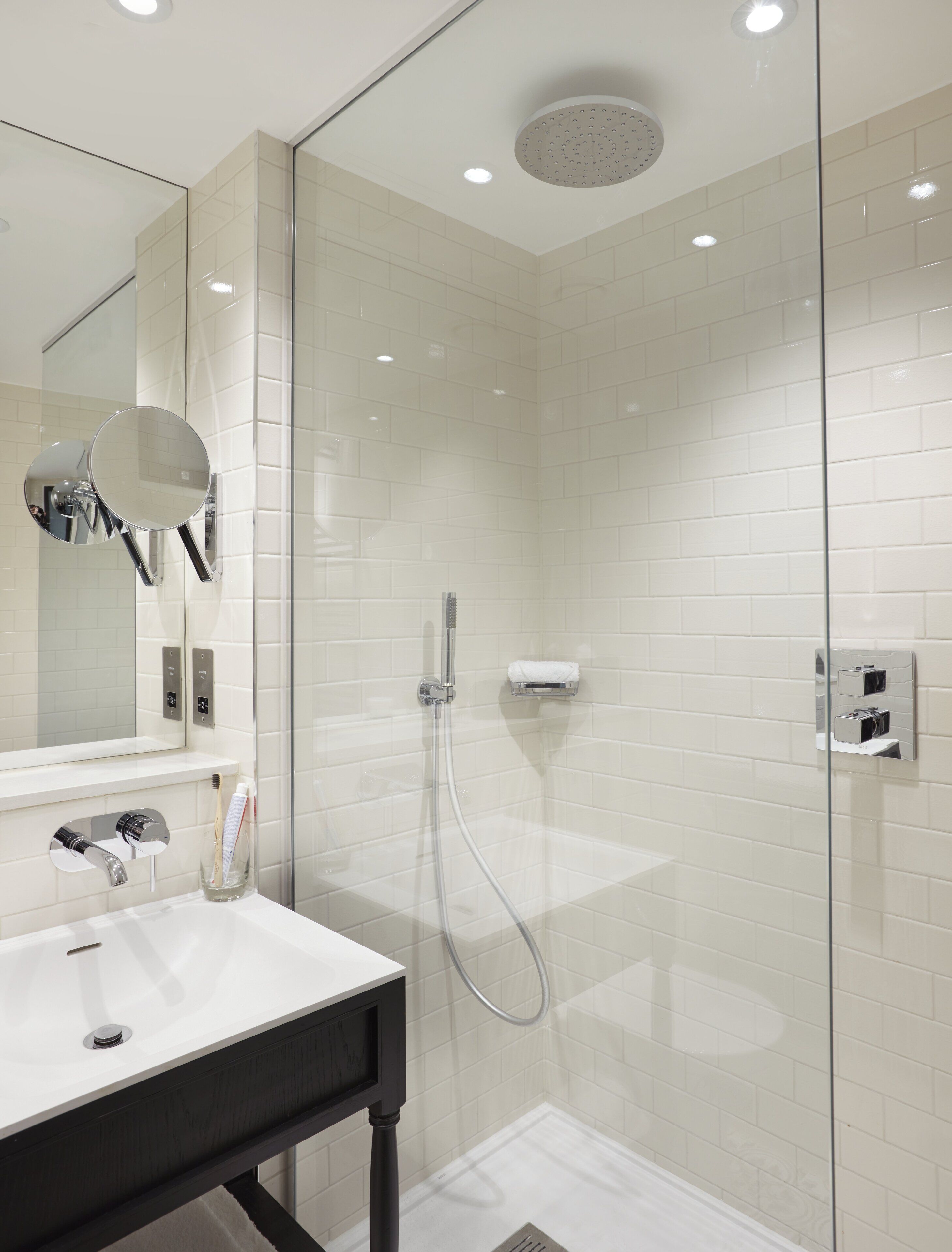 Un baño moderno con ducha de vidrio, un lavamanos blanco, un espejo y un perchero para toallas.