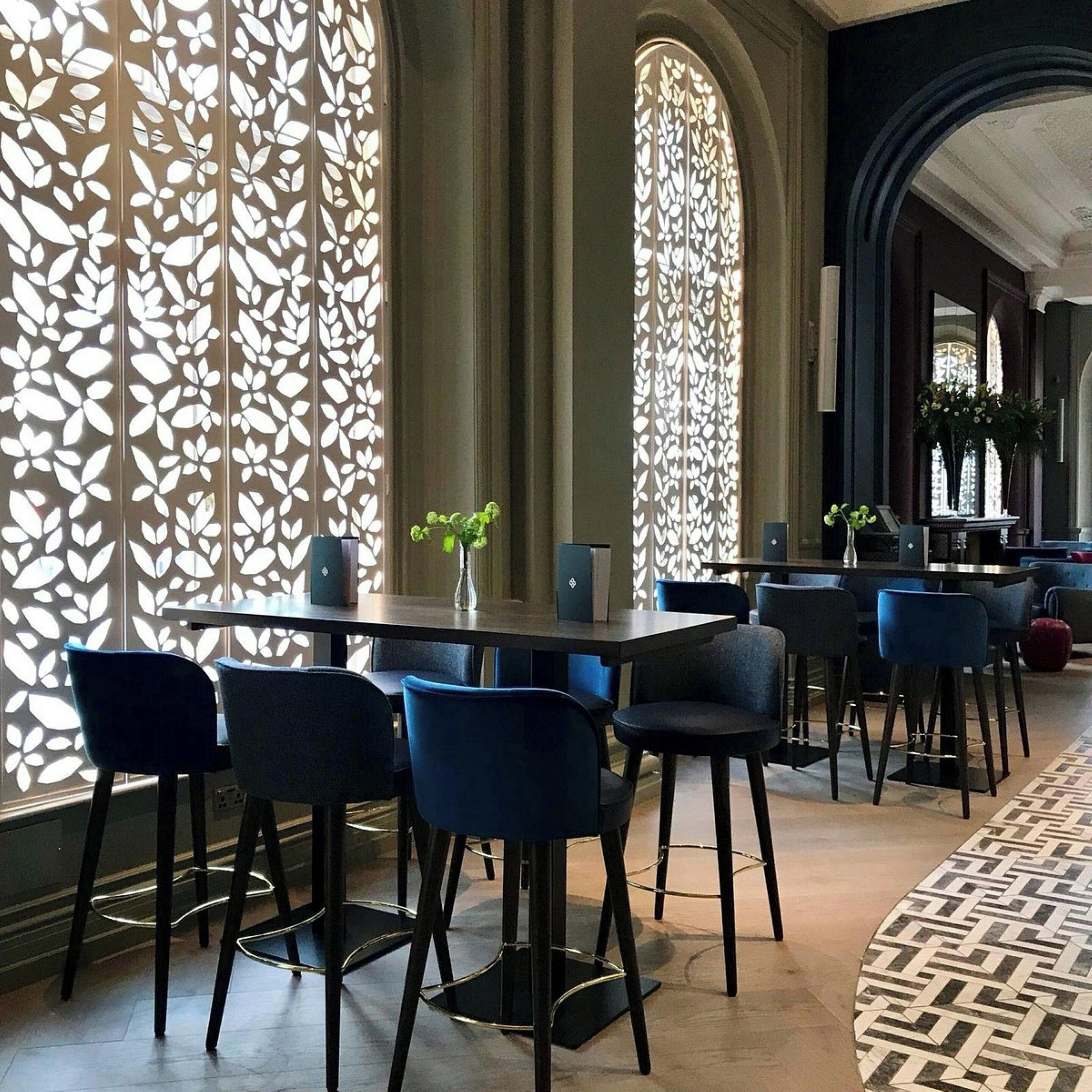 Un restaurante con una decoración moderna, que incluye un mamparo con diseño, sillas oscuras y un suelo estampado.