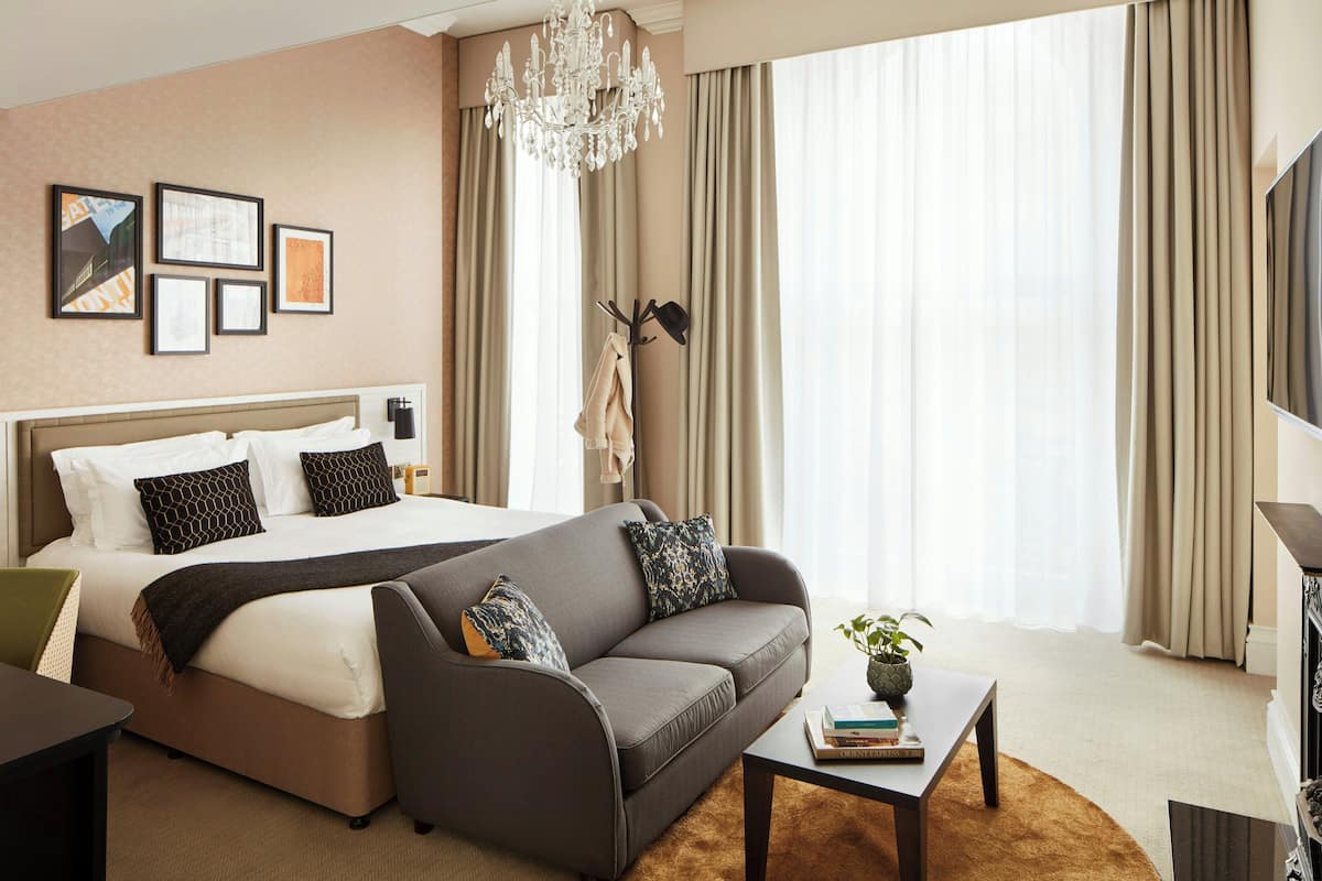 A hotel room with a bed, sofa, coffee table, TV, and artwork on the wall.