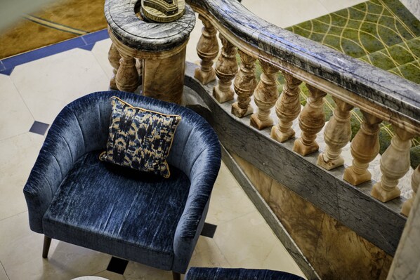 A blue velvet armchair with a patterned cushion, a marble column, and a wooden balustrade. - The Clermont London, Victoria (London)