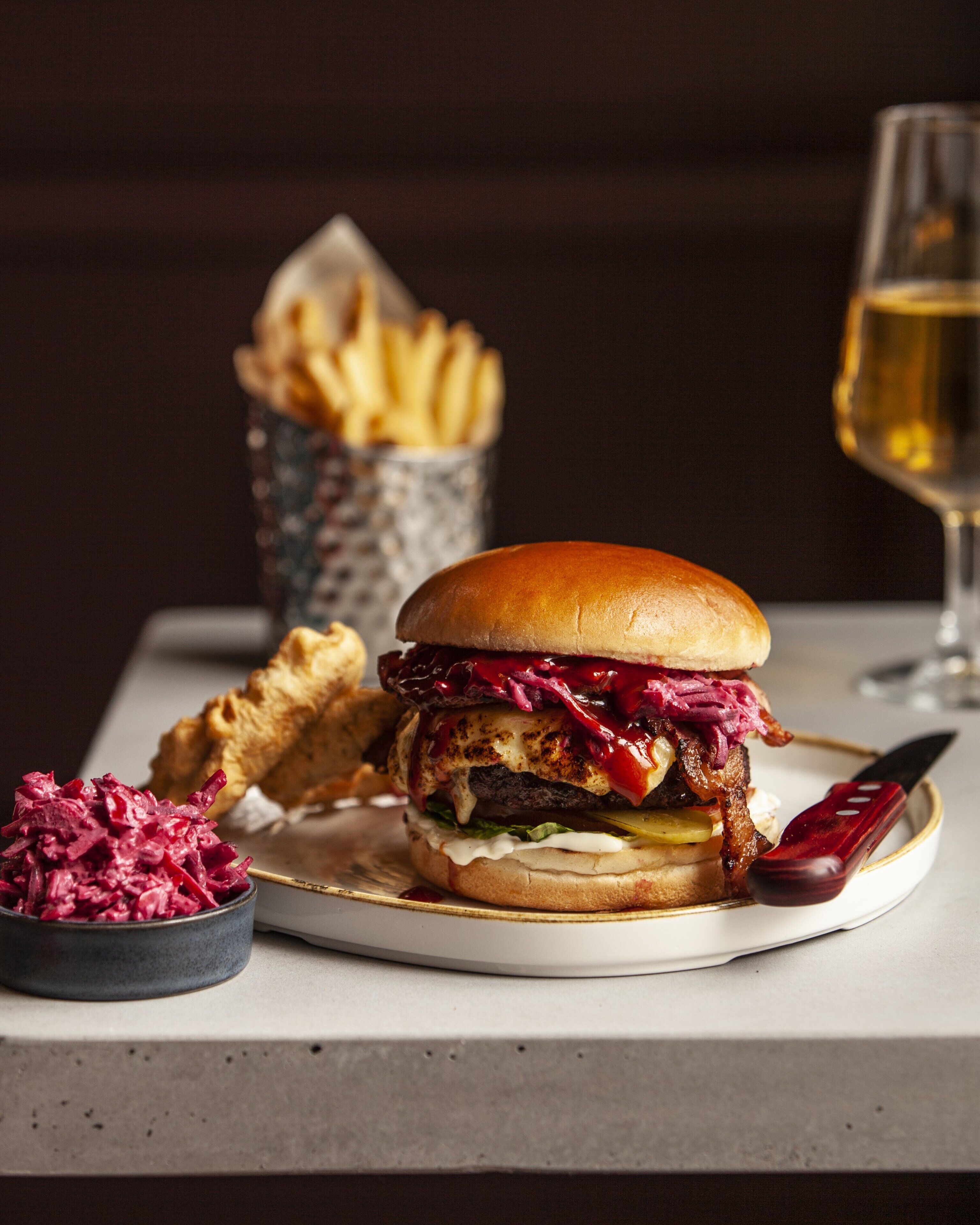 Una hamburguesa, papas fritas y una copa de vino sobre una mesa.