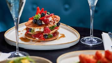 A dessert plate with pancakes topped with berries and syrup, accompanied by two champagne glasses on a table.