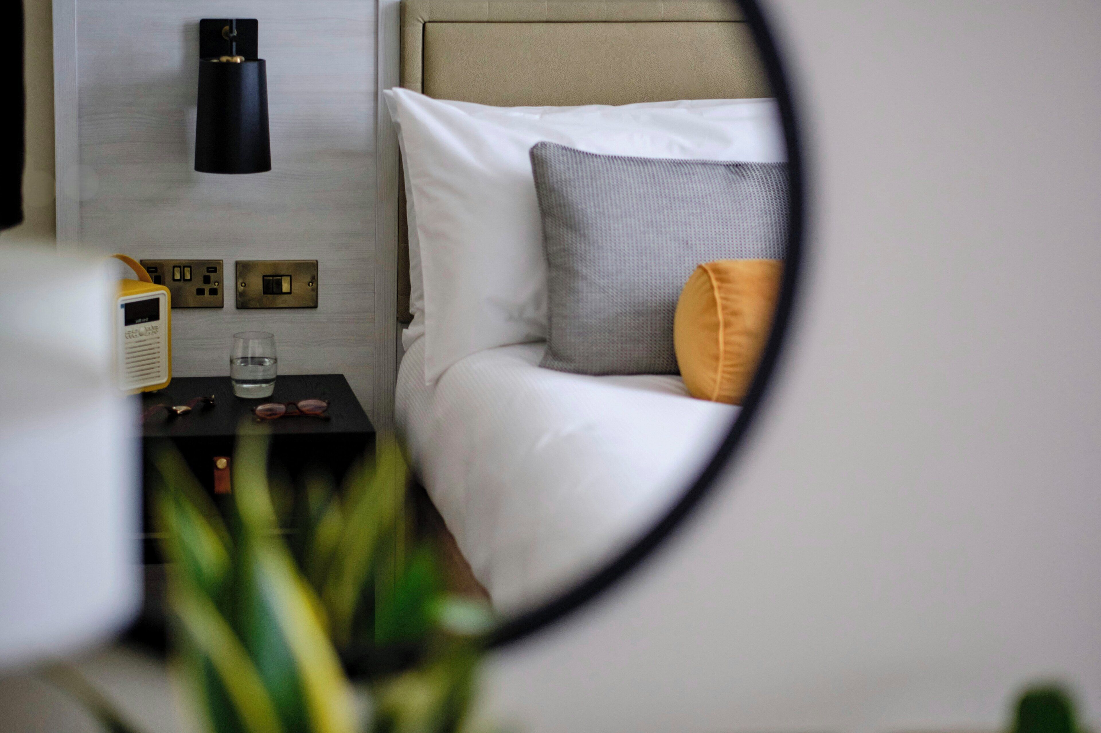 A bedroom with a bed, a bedside table with a radio, a glass, and a wall-mounted lamp.