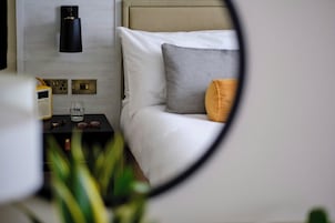 Ein Schlafzimmer mit einem Bett, einem Nachttisch mit Radio, einem Glas und einer Wandlampe.