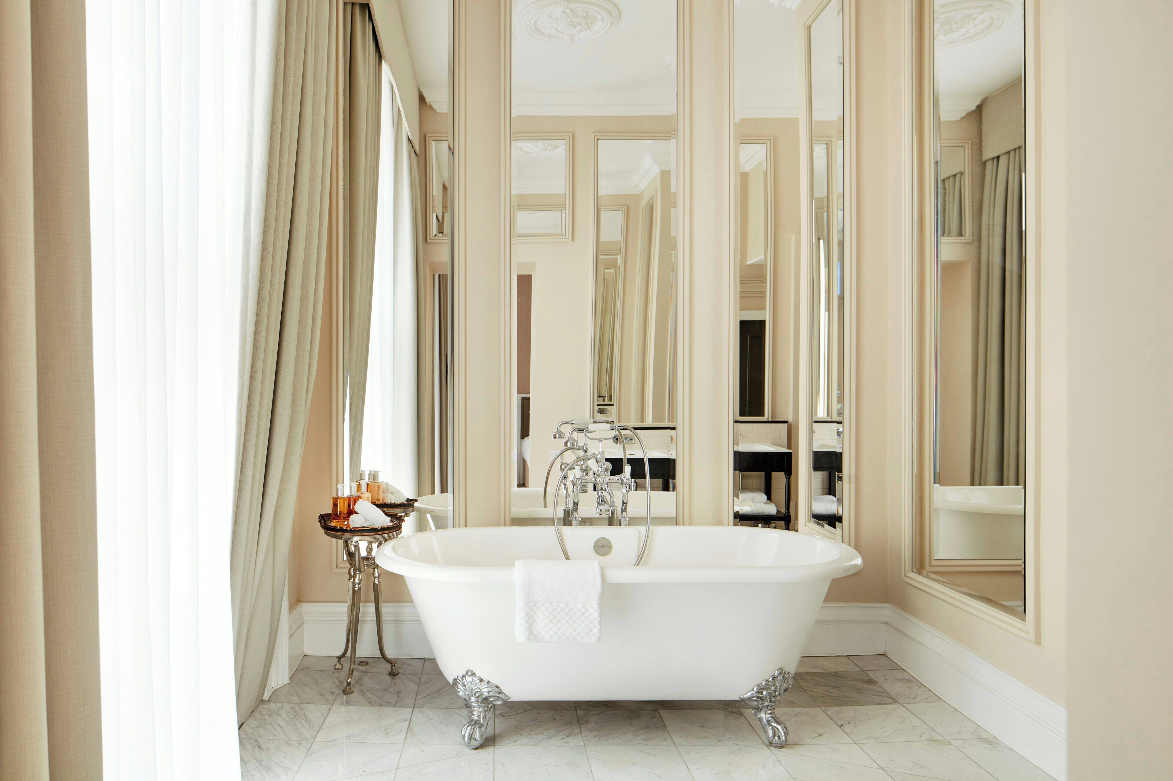 A bathroom with a freestanding bathtub, a vanity with a mirror, and a small table with toiletries.
