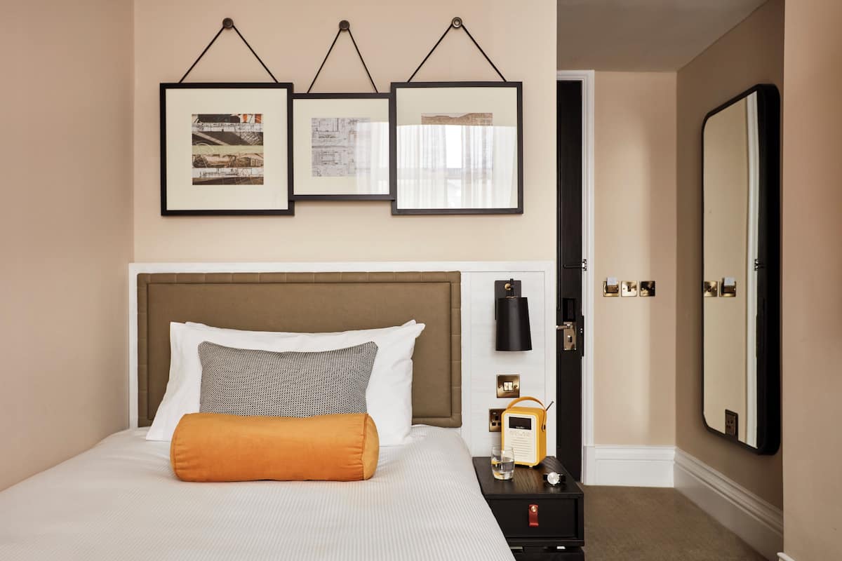 A hotel room with a bed, bedside table, radio, and framed pictures on the wall.