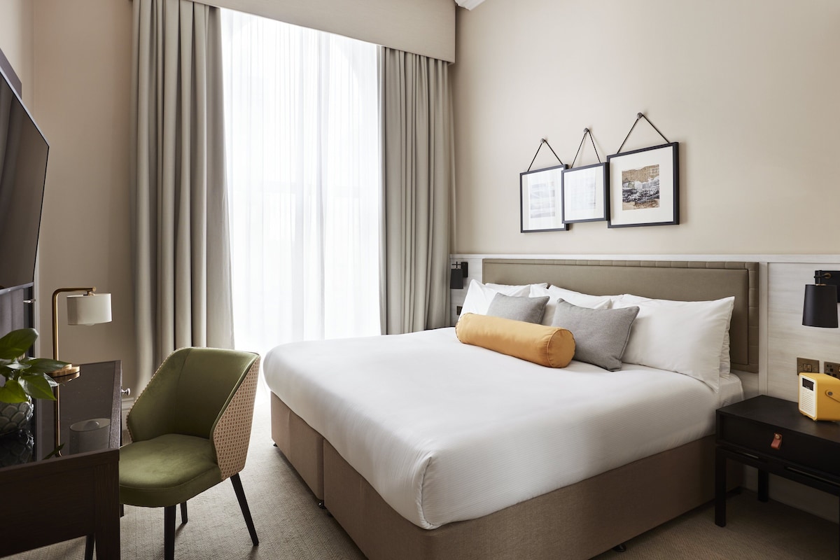 Een hotelkamer met een groot bed, een bureau met lamp, een stoel en een televisie.