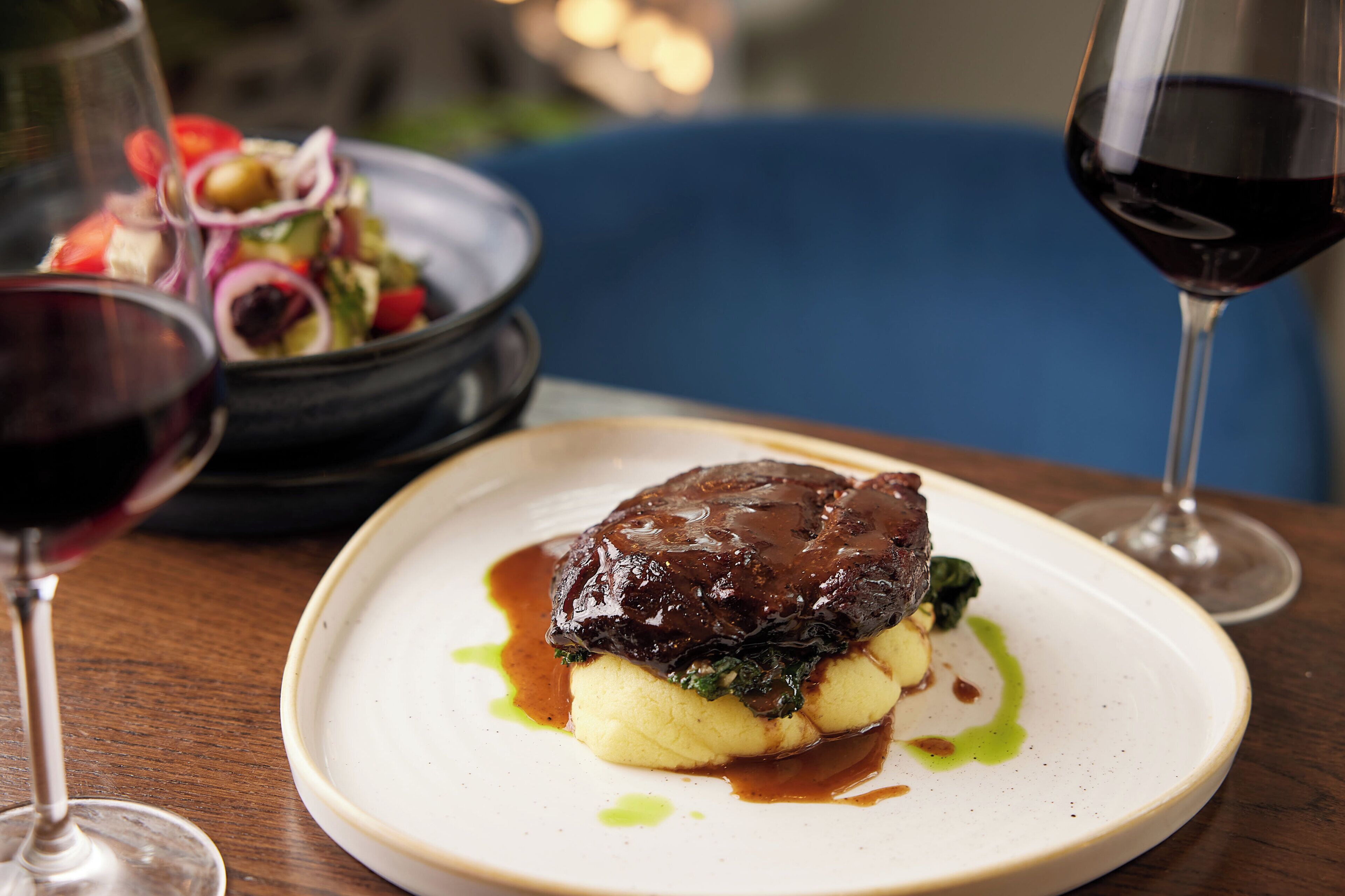 A plate of food with a meat dish and mashed potatoes, accompanied by a glass of red wine.