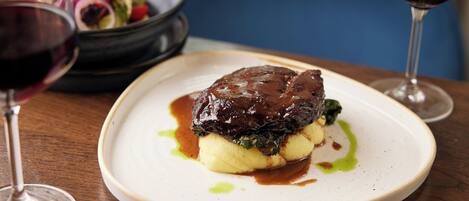 A plate of food with a meat dish and mashed potatoes, accompanied by a glass of red wine.