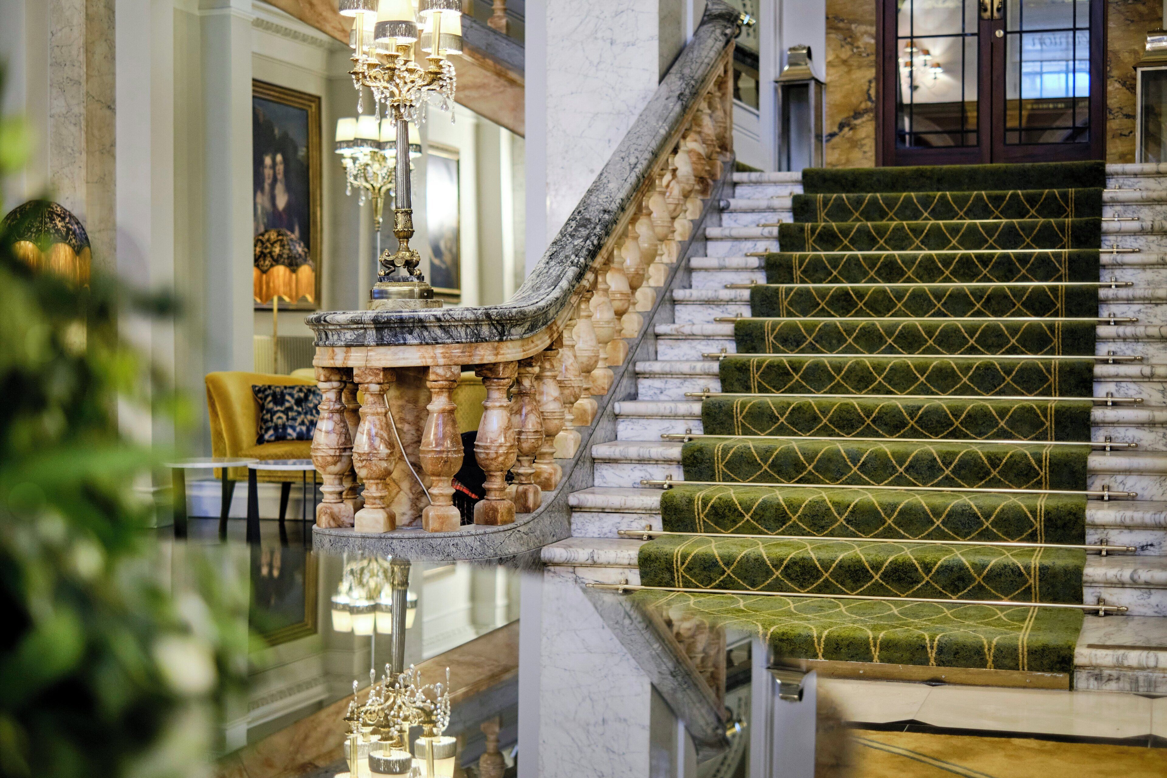 Un magnifique escalier avec des marches recouvertes d’une moquette verte et une balustrade en marbre.