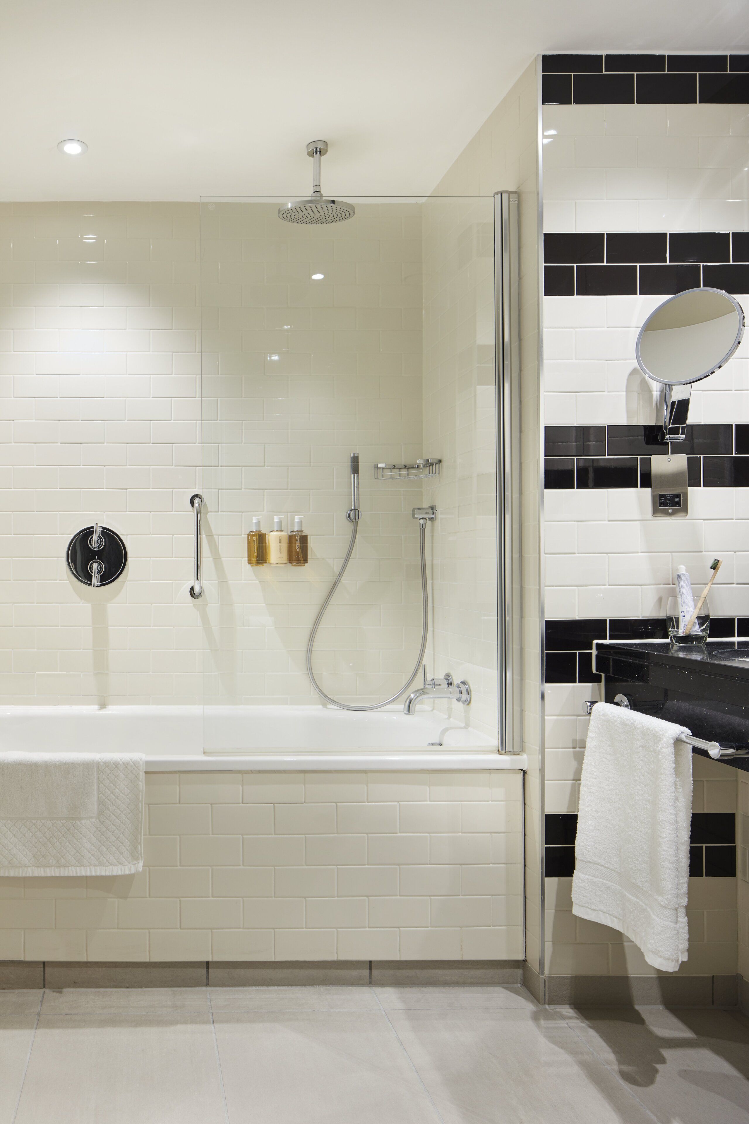 A modern bathroom with a glass-enclosed shower, a white bathtub, and a black and white tiled wall.