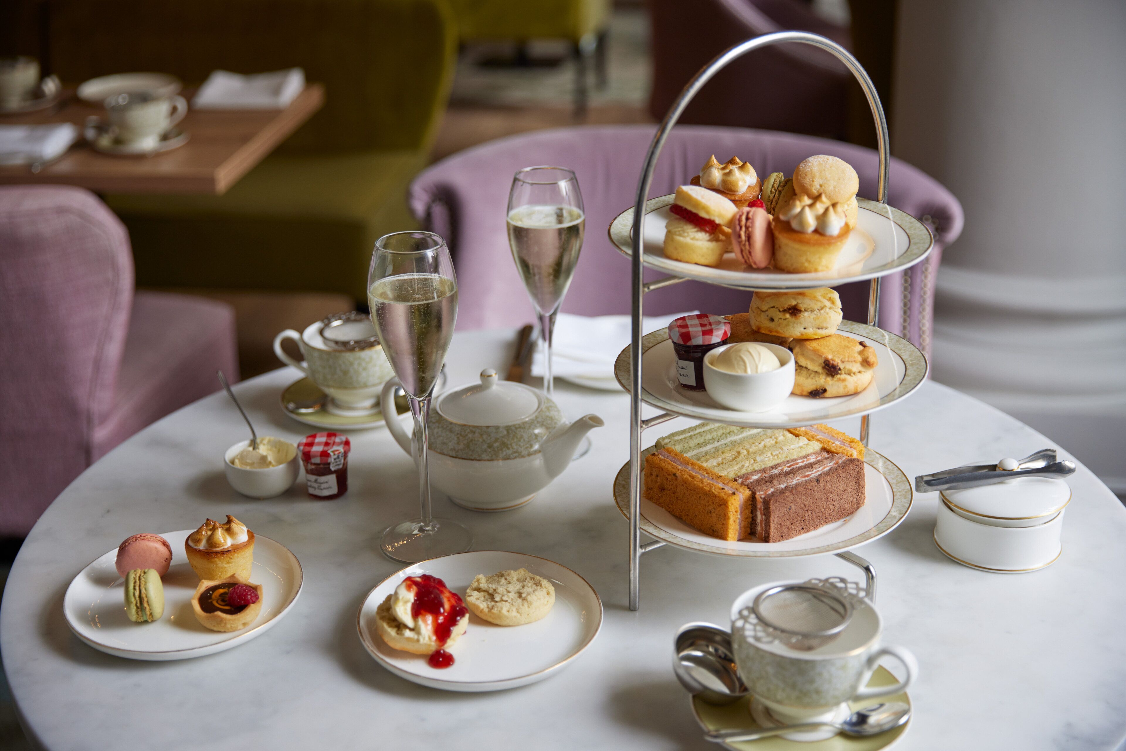 A tea service set with a tiered tray, teapot, cups, and saucers on a round table.