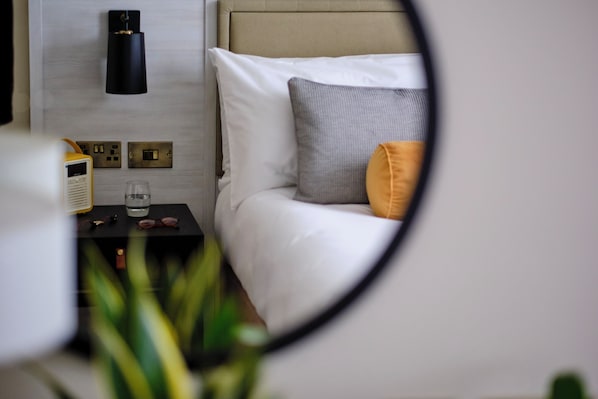A bedroom with a bed, a bedside table with a radio, a glass, and a plant.