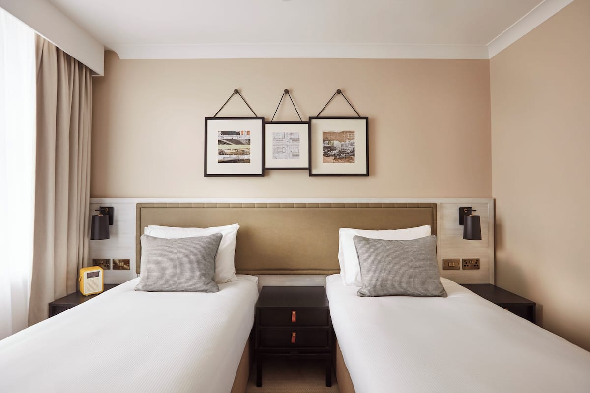 A hotel room with two beds, a headboard, bedside tables, a radio, and framed pictures on the wall.